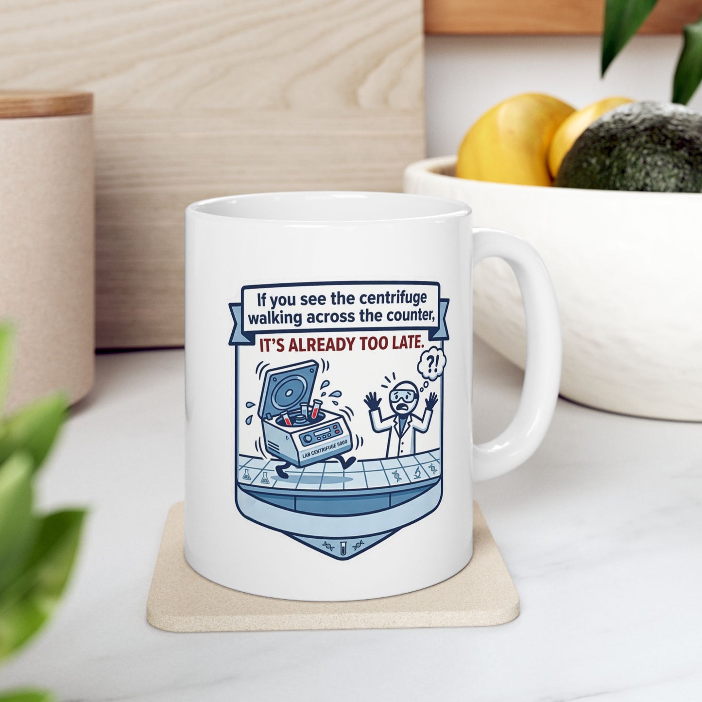 White mug with a humorous design and text on a coaster, placed on a surface with a plant and container in the background.